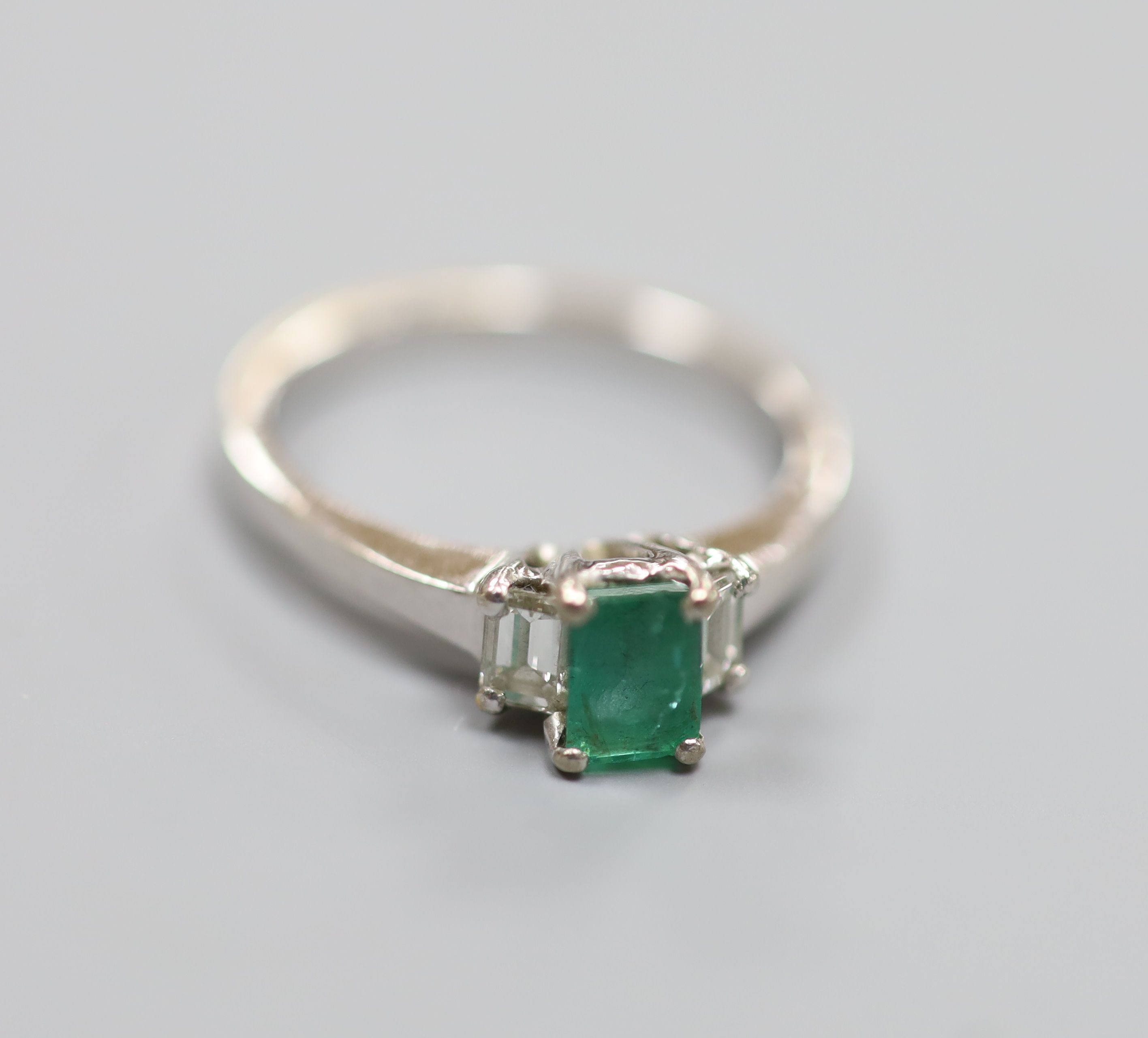 A modern white metal (engraved 750), emerald and diamond set three stone ring, size P